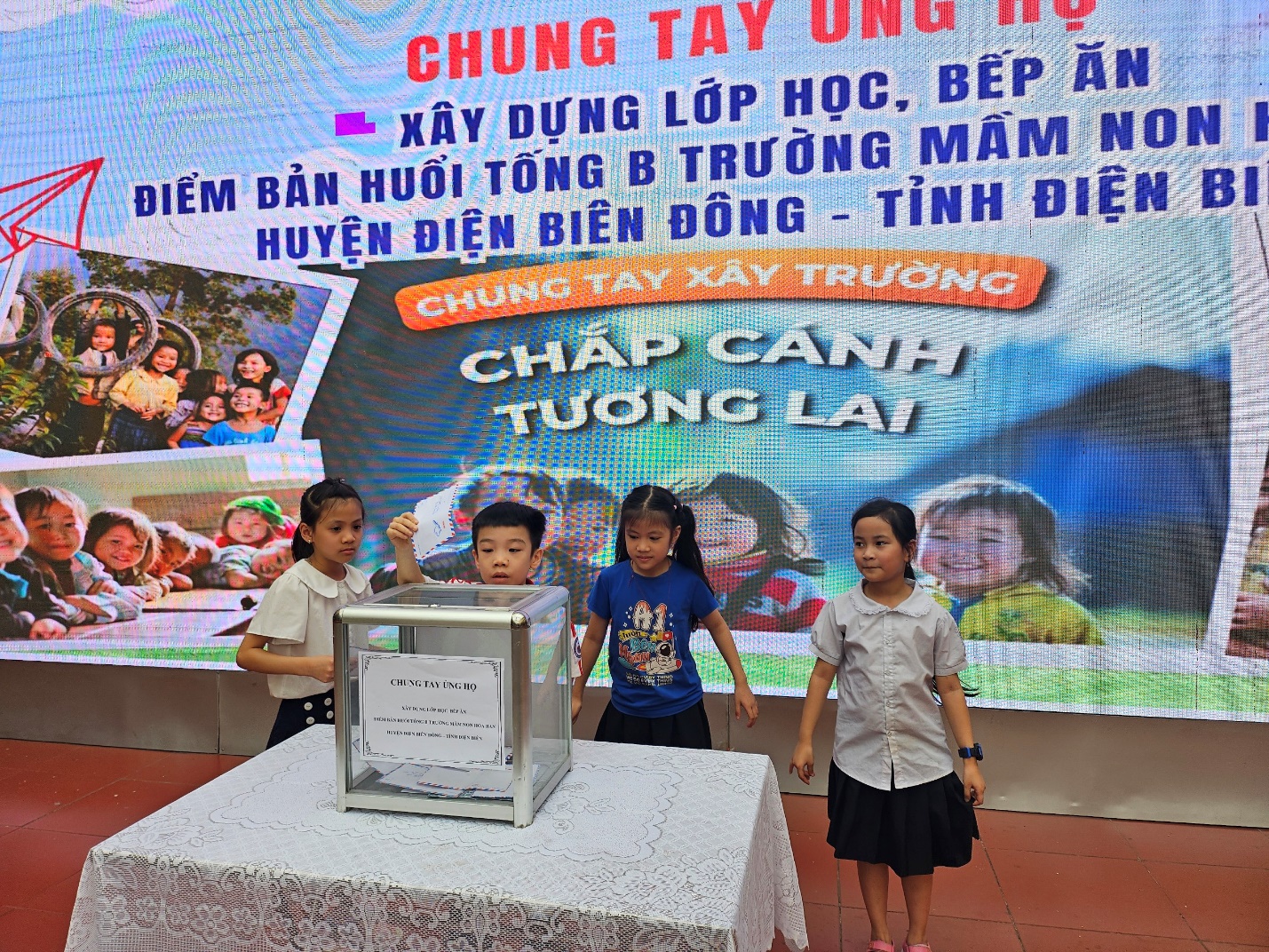 A group of children standing next to a large screen

Description automatically generated